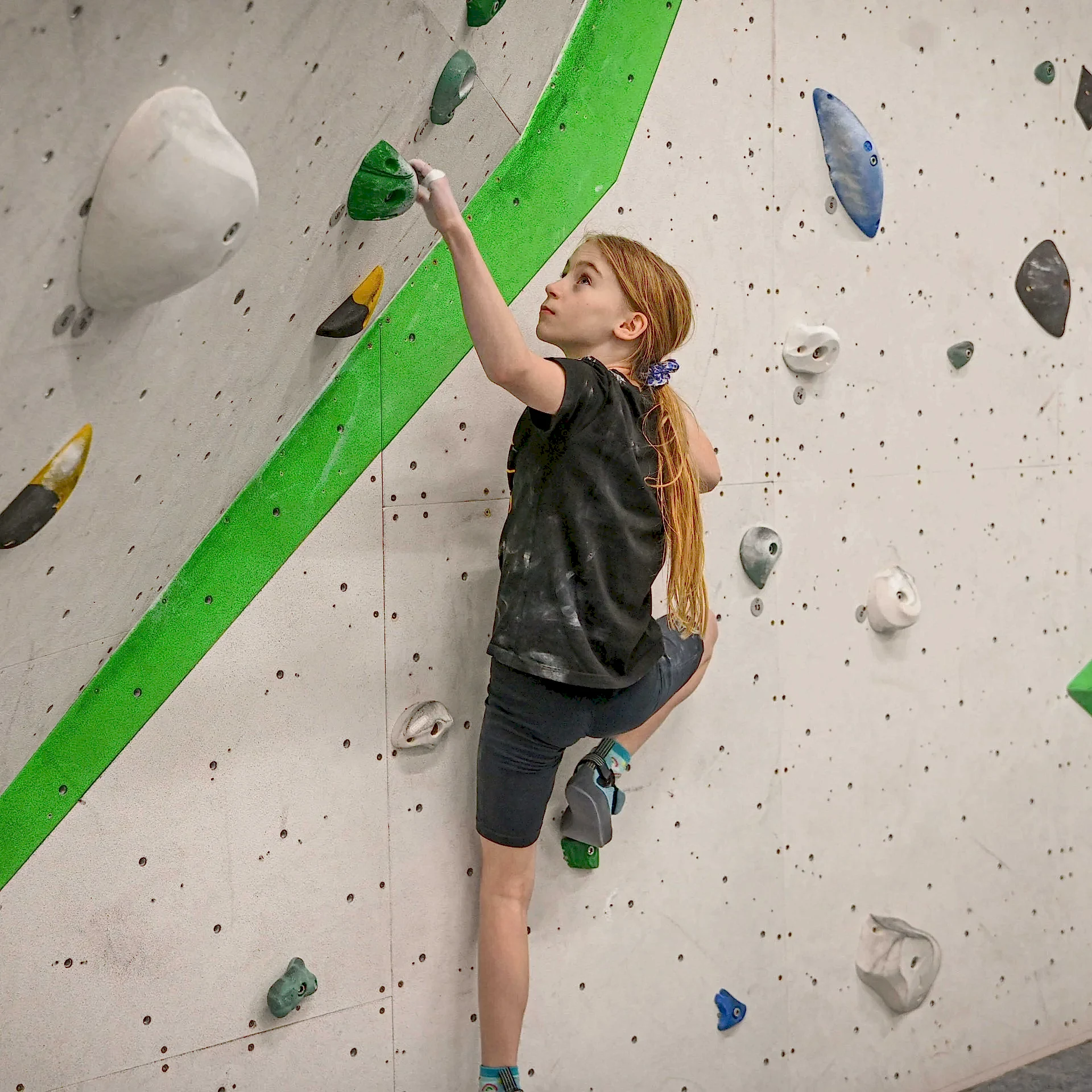 Girl climbing an indoor rock climbing wall, looking up to the next hold at RavensWall.